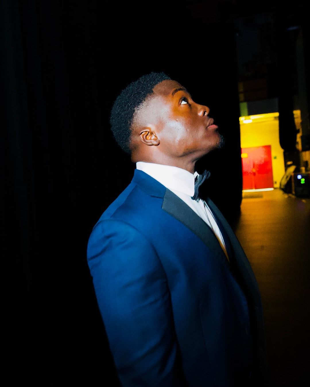 Call Me Manny in a blue tuxedo, looking toward the spotlight